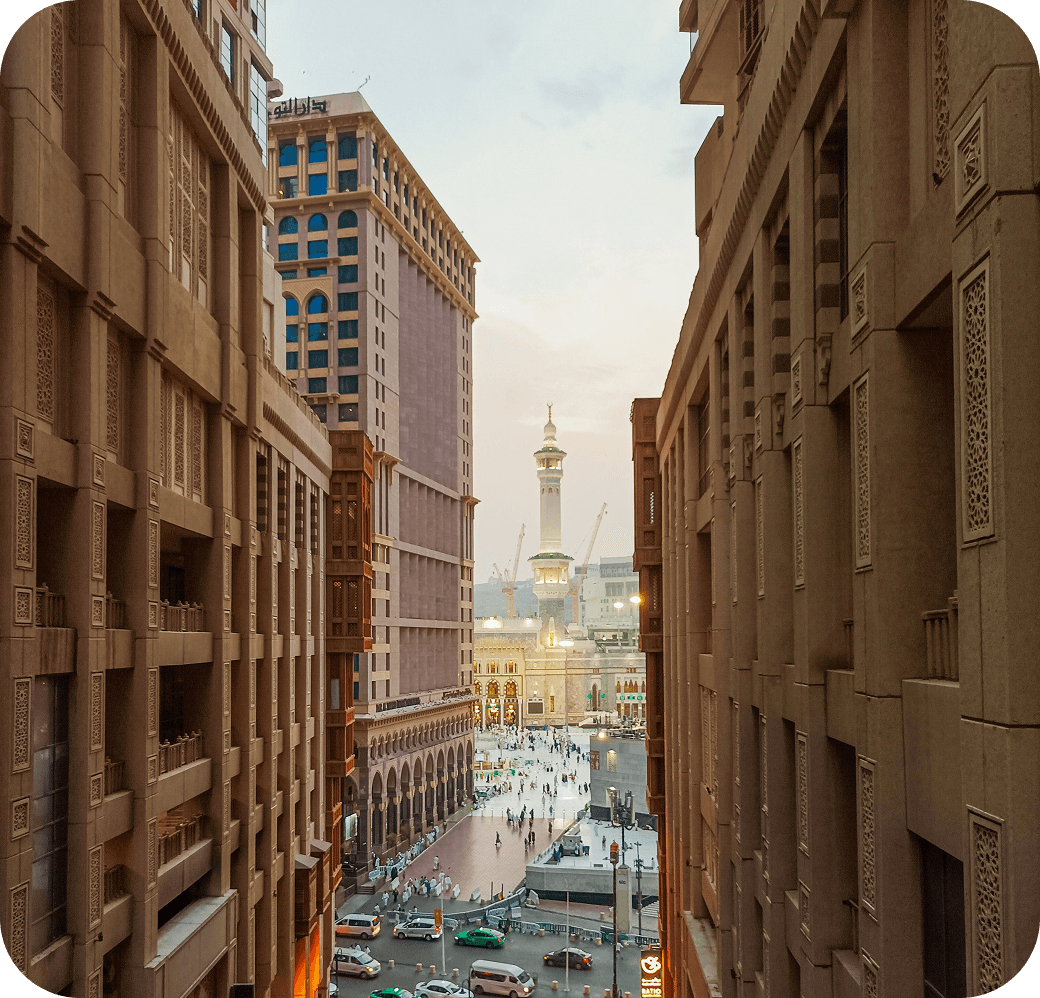 A Makkah street canyon at dusk, opening onto the Haram and its minarets